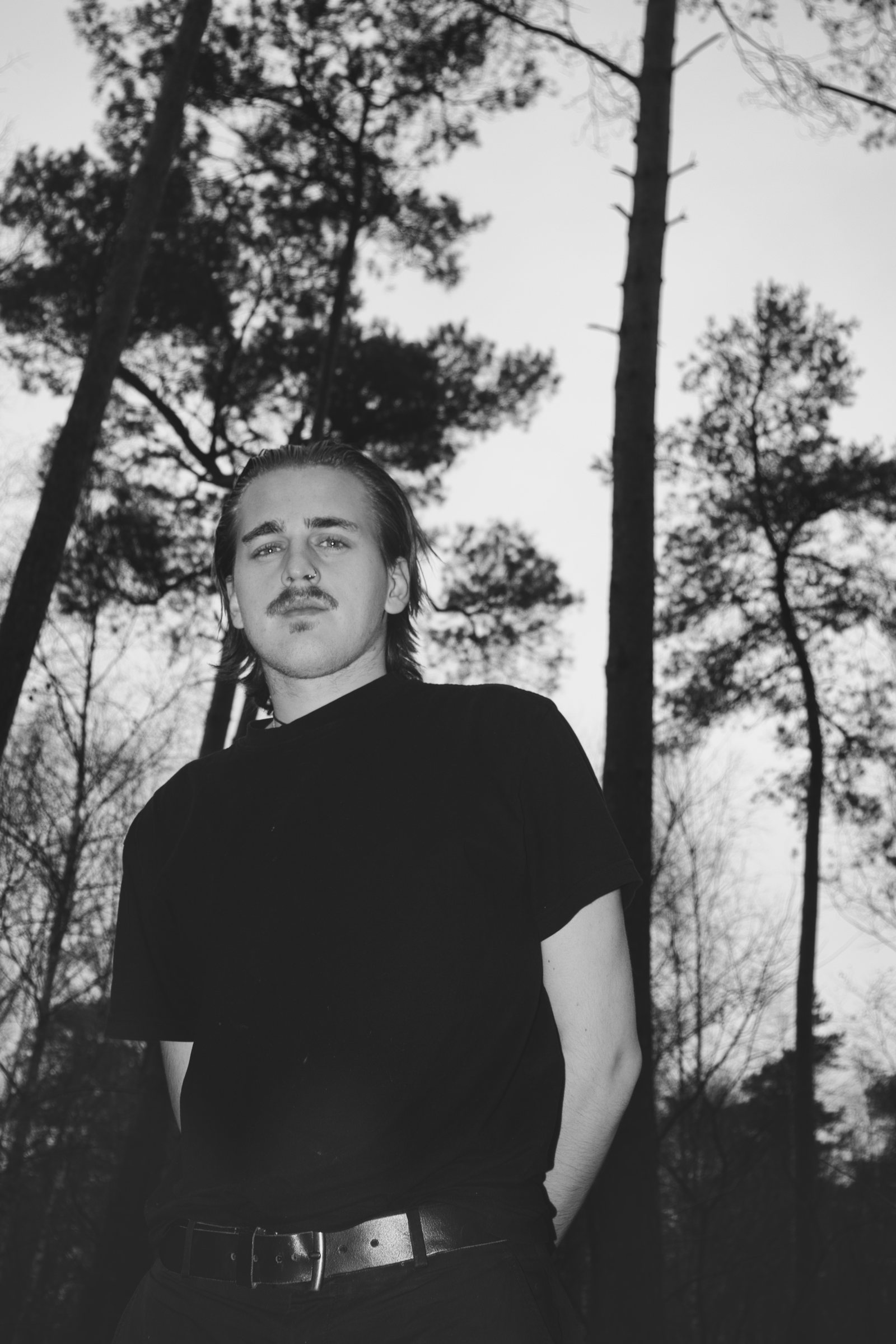 Black and white low-angle portrait of FLAWS standing among tall trees.
